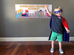 Boy dressed as a superhero in front of a superhero banner